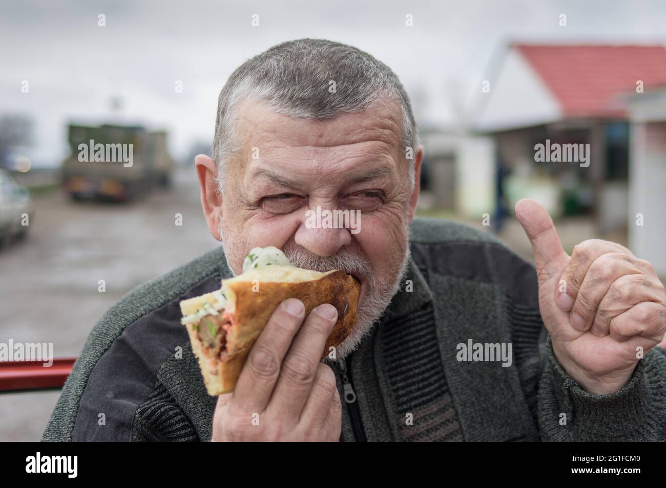 Ritratto di affamato pilota caucasico senior mangiare lyulya kebab in lavash vicino alla sua auto Foto Stock