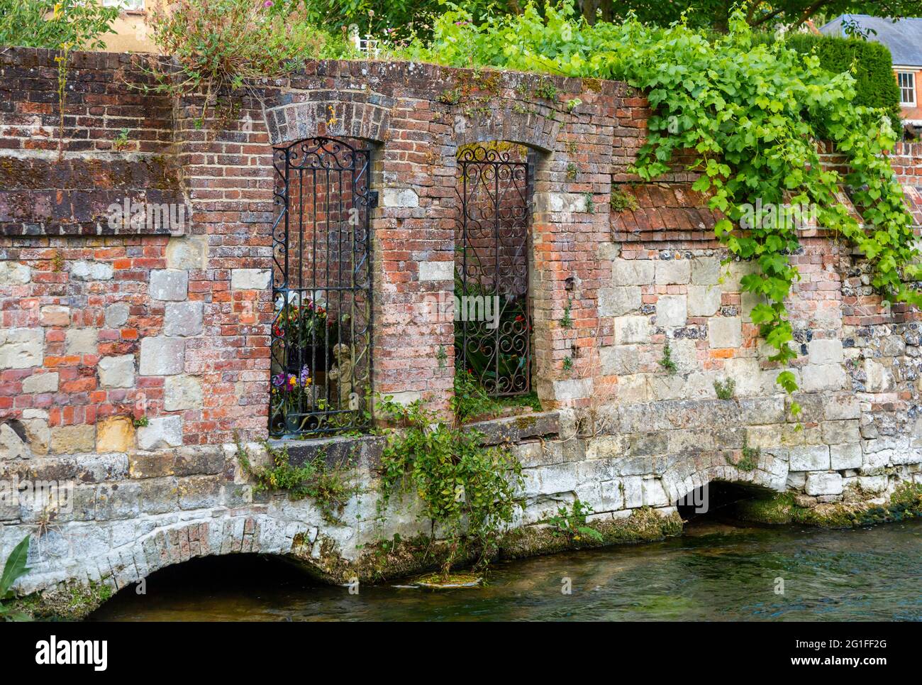 Cancelli in ferro battuto in un vecchio muro di mattoni rossi che conduce dai giardini al fiume Itchen nei Weirs, Winchester, Hampshire Foto Stock