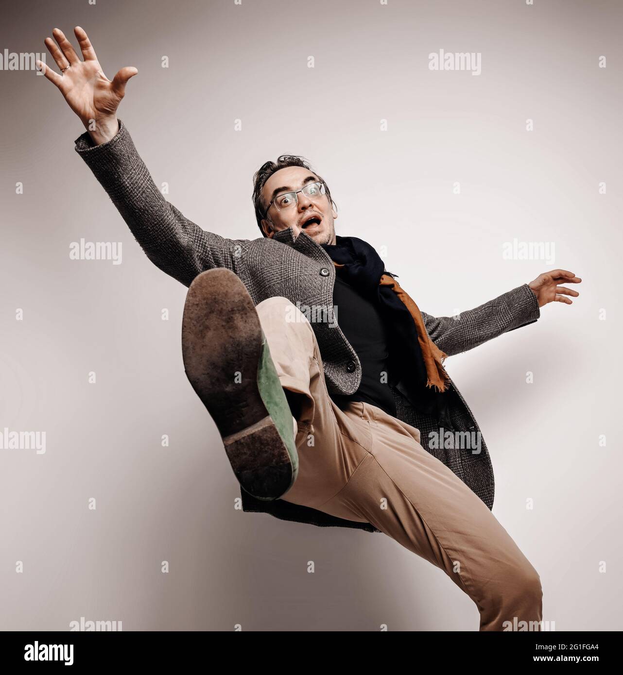 Uomo adulto stupefatto in pantaloni e giacca di plaid si alza il piede, facendo un passo gigante, cadendo giù le mani ondeggianti Foto Stock