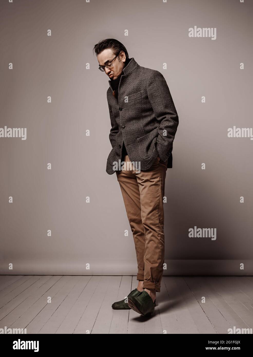 Ritratto di un uomo adulto intellettuale snobbato in giacca a scacchi e sciarpa nera che guarda verso il basso la suola della sua scarpa Foto Stock