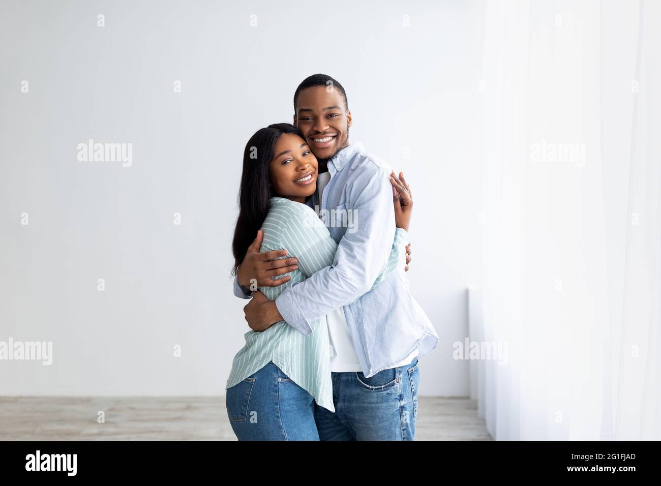 Coppia afro-americana amorevole in piedi nella loro casa, abbracciando e sorridendo, essendo felice di acquistare un proprio alloggio Foto Stock