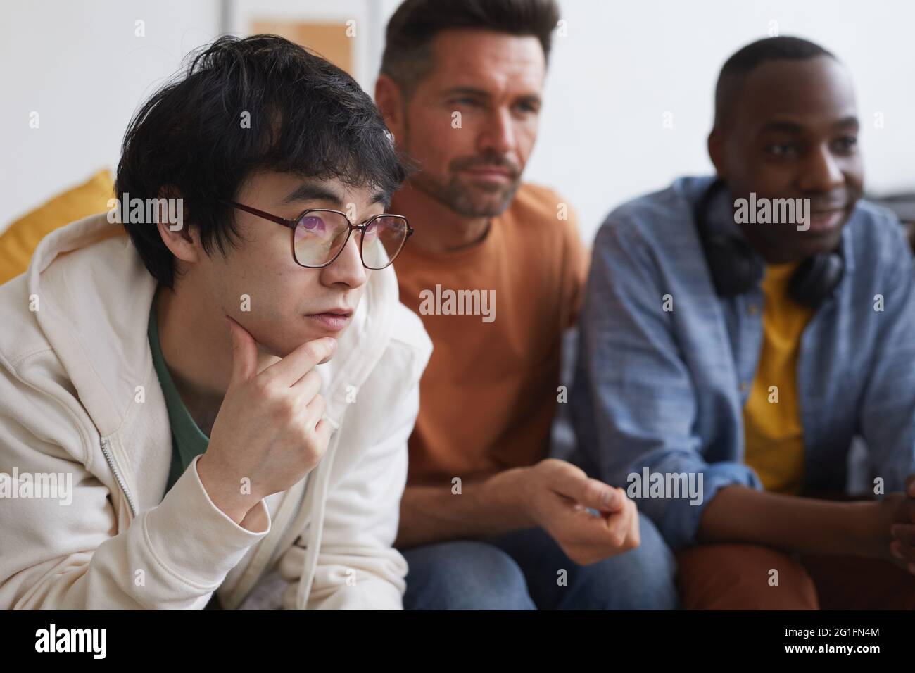 Gruppo multietnico di amici che guardano la TV a casa insieme mentre si siede in fila sul divano, spazio per la copia Foto Stock