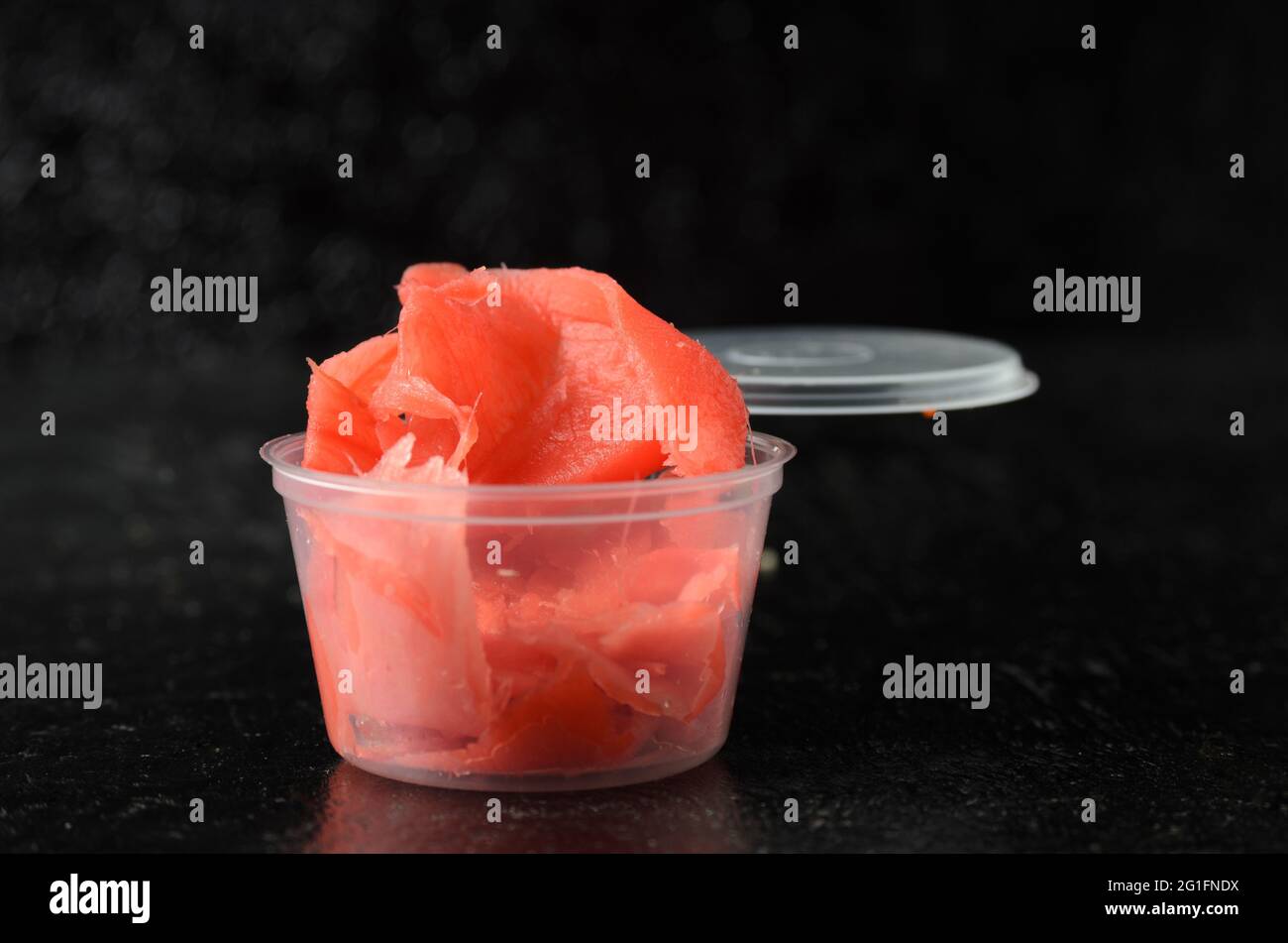Radice di zenzero tagliata a fette sottili di colore rosso in un vaso di plastica di consegna. Messa a fuoco selettiva. Foto Stock