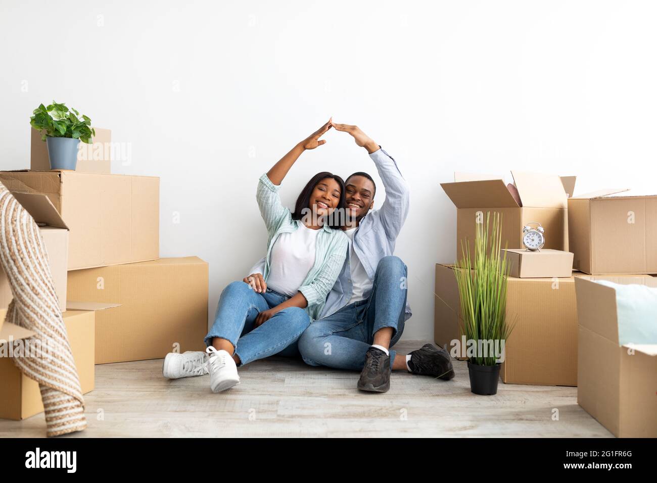 Ipoteca per famiglie giovani. Felice coppia nera che si sposta nella propria casa, unendosi le mani rendendo simbolico tetto della casa Foto Stock