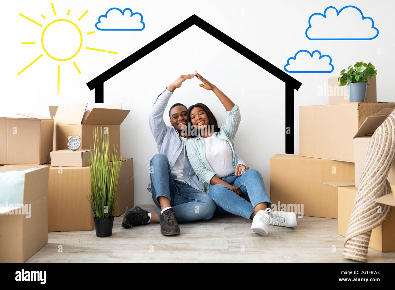 Coppia afro-americana amorevole che si sposta a casa propria, unendo le mani tra scatole di cartone vicino al muro con la casa disegnata Foto Stock