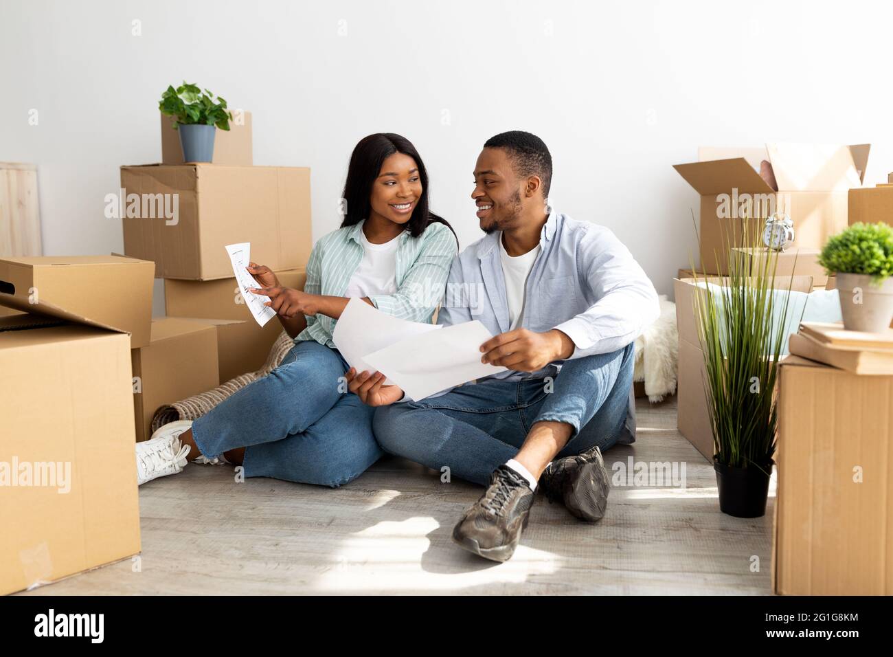 Famiglia giovane amorevole che pensa al disegno domestico, che tiene il programma dell'appartamento, seduto sul pavimento fra le scatole con gli effetti personali, Foto Stock