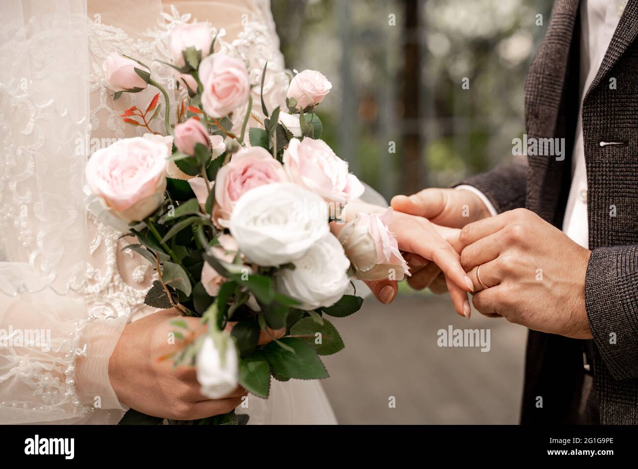 vista tagliata della donna con bouquet di nozze vicino allo sposo mettendo l'anello di nozze sul suo dito Foto Stock