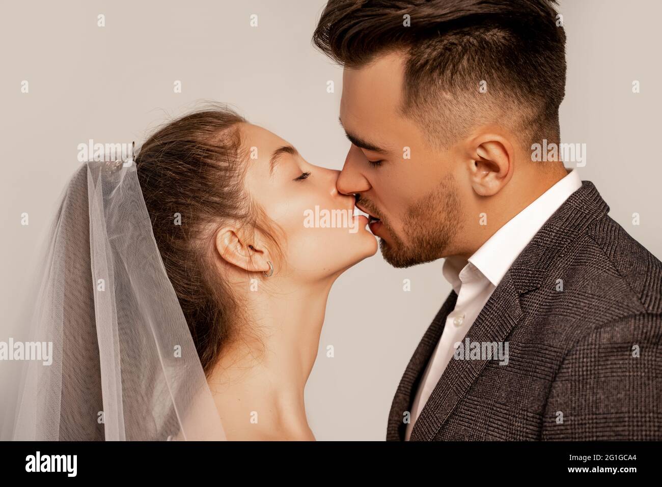 vista laterale di giovani sposi che baciano con occhi chiusi isolati su grigio Foto Stock