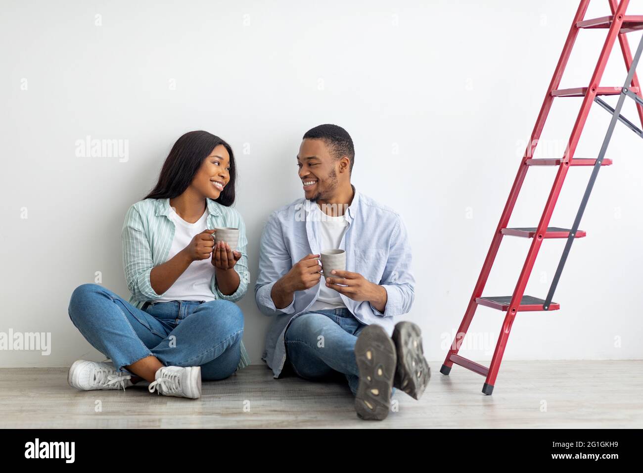 Giovane coppia afroamericana che discute di un piano di riparazione nella loro nuova casa e beve caffè, seduto a terra Foto Stock