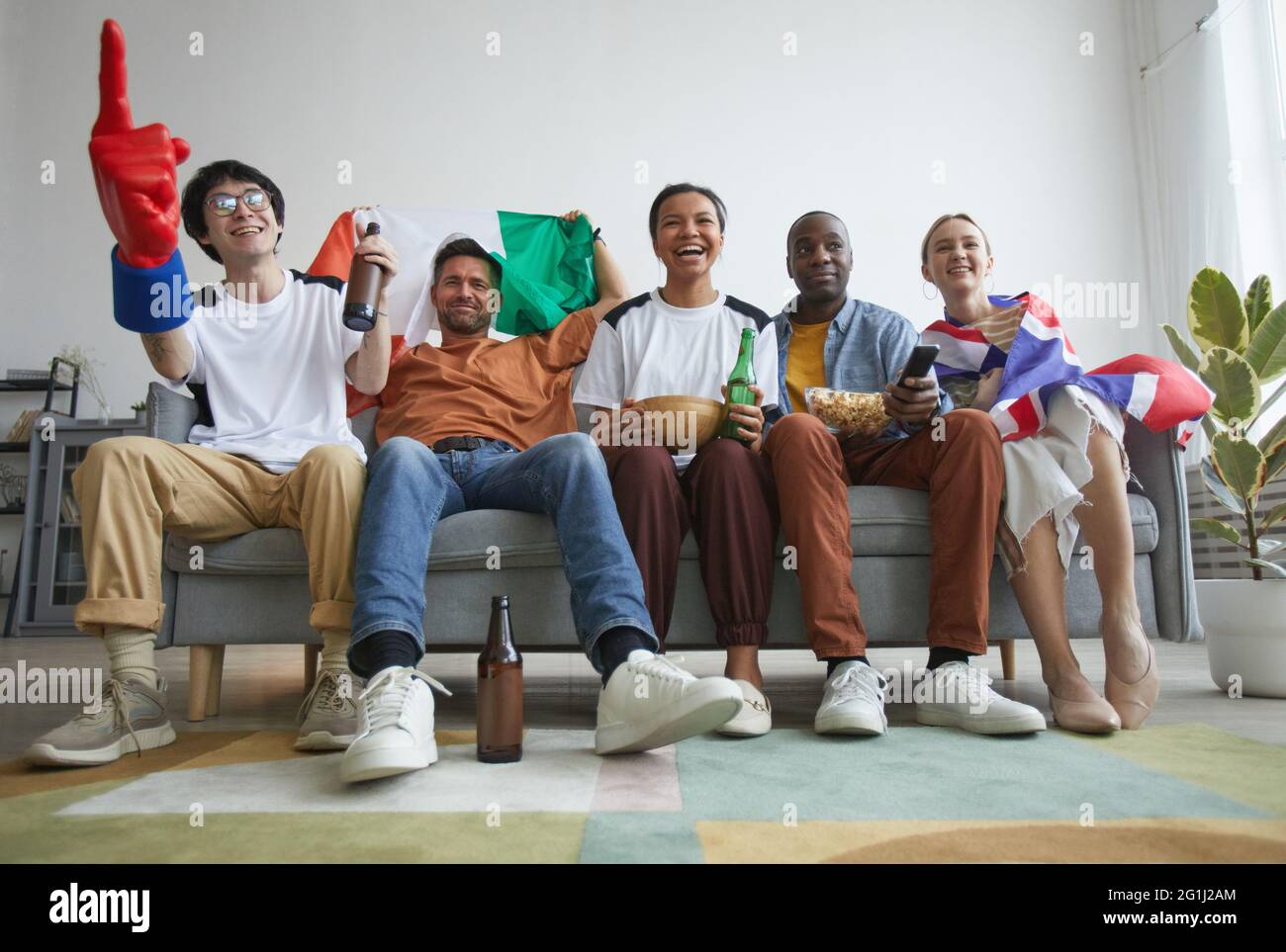 Vista dall'angolo basso a un gruppo eterogeneo di appassionati di sport che guardano partite a casa e che si acclamano con gioia Foto Stock