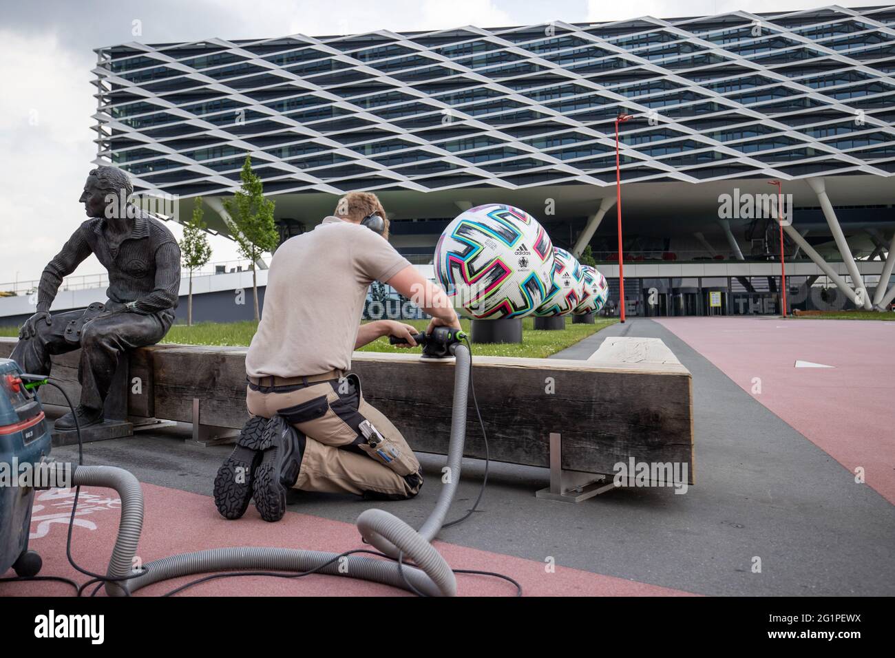 Herzogenaurach, Germania. 07 giugno 2021. Di fronte all'edificio degli uffici 'Arena', nei locali del produttore di articoli sportivi adidas, un falegname macina una panchina di legno sulla quale è collocata una statua del fondatore Adolf 'Adi' Dassler. Sullo sfondo c'è un pallone ufficiale oversize 'Uniforia' di EURO 2020. La squadra nazionale tedesca di calcio e il personale di supporto soggiorneranno presso il "Home Ground" presso la sede del partner DFB adidas per tutta la durata del Campionato europeo. Credit: Daniel Karmann/dpa/Alamy Live News Foto Stock