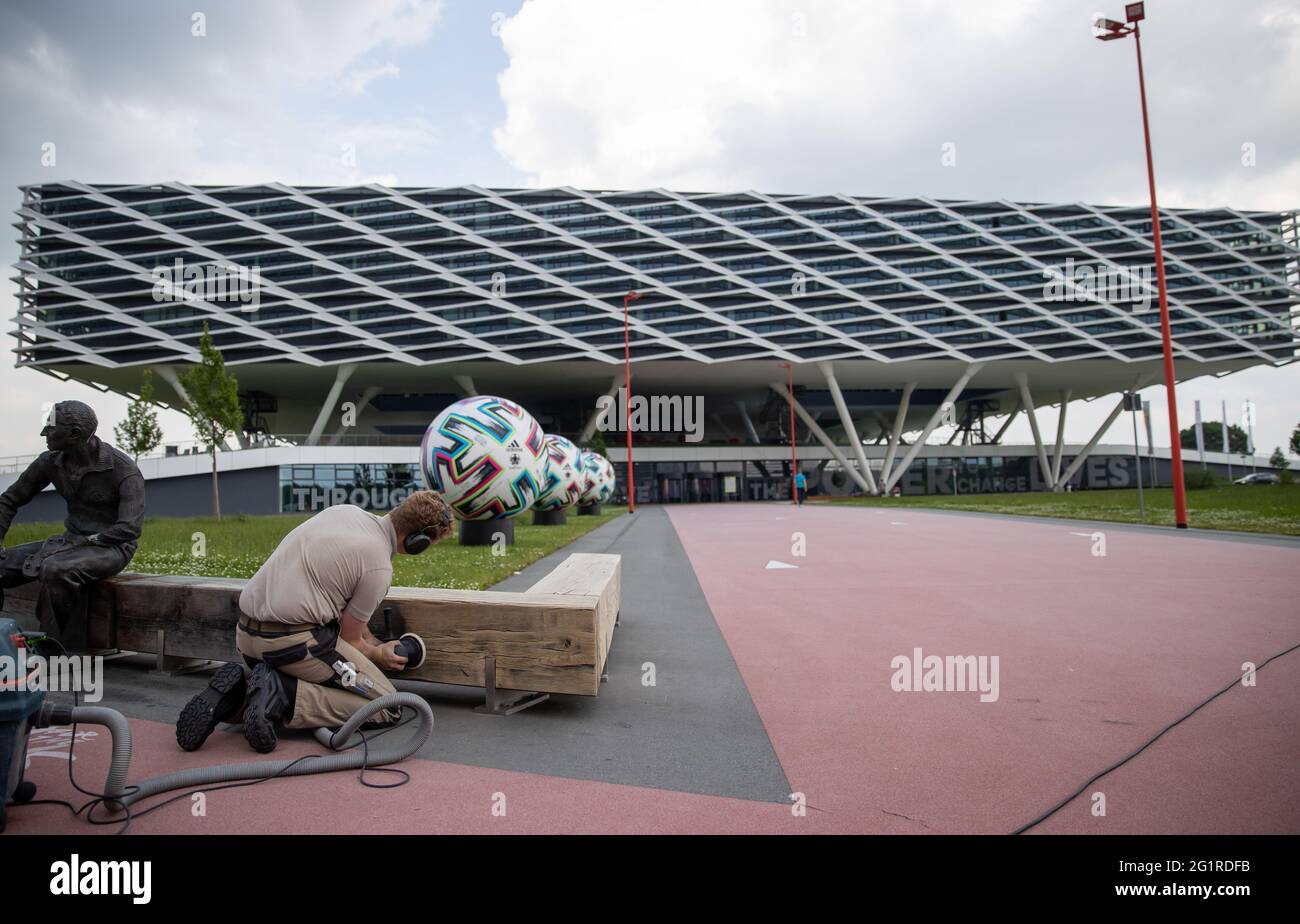 07 giugno 2021, Bavaria, Herzogenaurach: Di fronte all'edificio degli uffici 'Arena' nei locali del produttore di articoli sportivi adidas, un falegname macina una panchina di legno sulla quale è collocata una statua del fondatore Adolf 'Adi' Dassler. Sullo sfondo c'è un pallone ufficiale oversize 'Uniforia' di EURO 2020. La squadra nazionale tedesca di calcio e il personale di supporto soggiorneranno presso il "Home Ground" presso la sede del partner DFB adidas per tutta la durata del Campionato europeo. Foto: Daniel Karmann/dpa Foto Stock