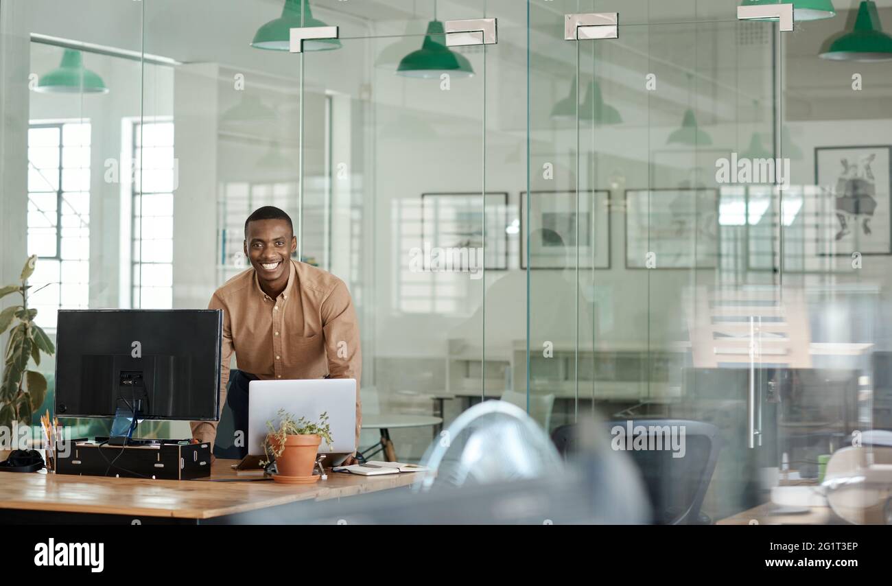 Sorridente uomo d'affari africano che lavora sulla sua scrivania in un ufficio Foto Stock
