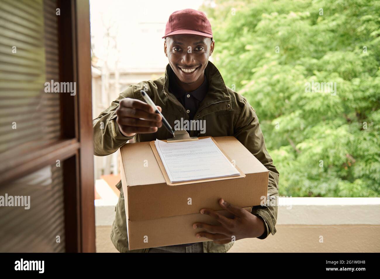 Sorridente corriere africano che tiene una clipboard per firmare per una consegna Foto Stock