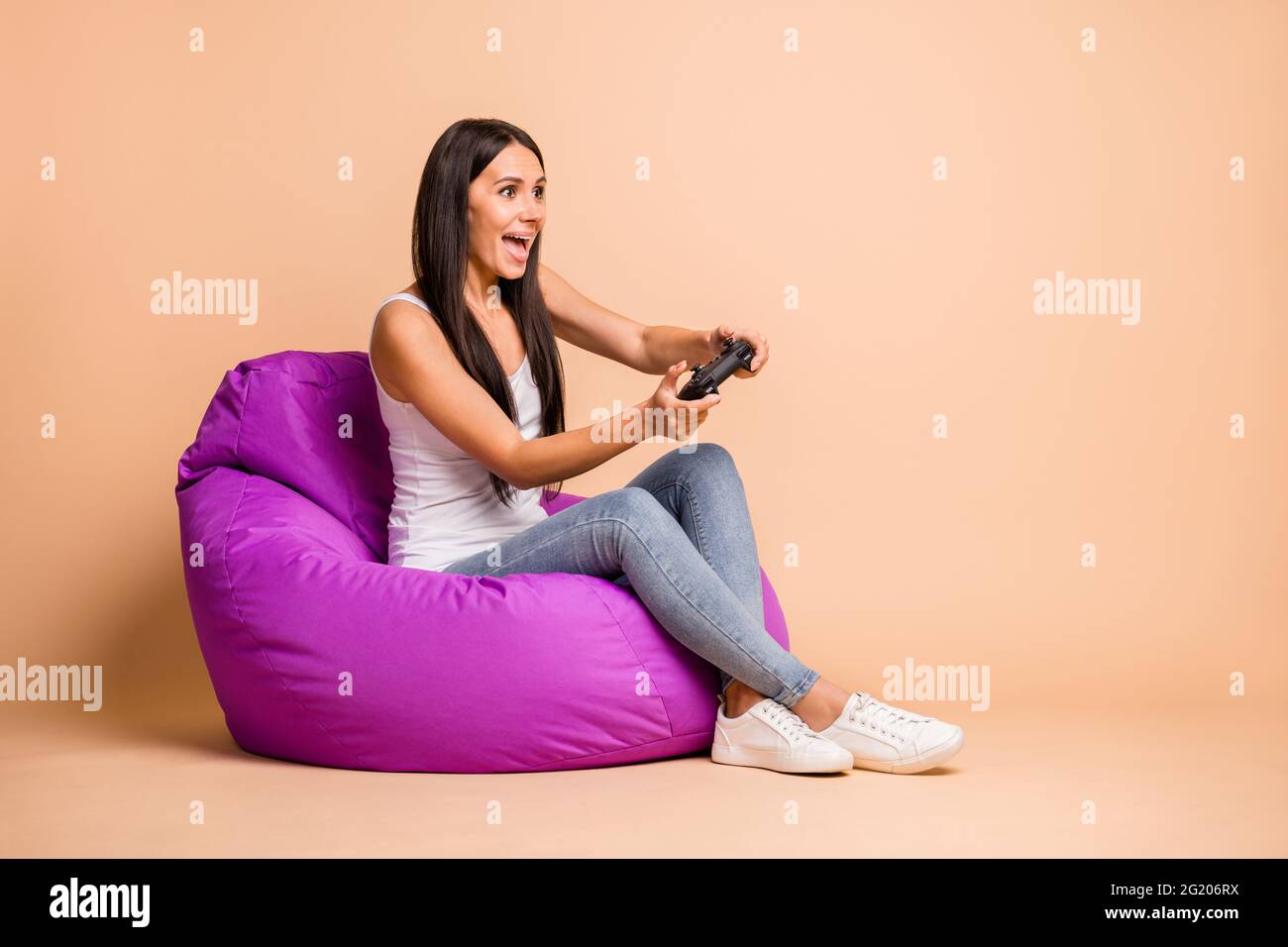 Foto profilo a dimensione intera della pouf ottimista della bruna girl sit con jeans playstation Wear top isolati su sfondo beige Foto Stock