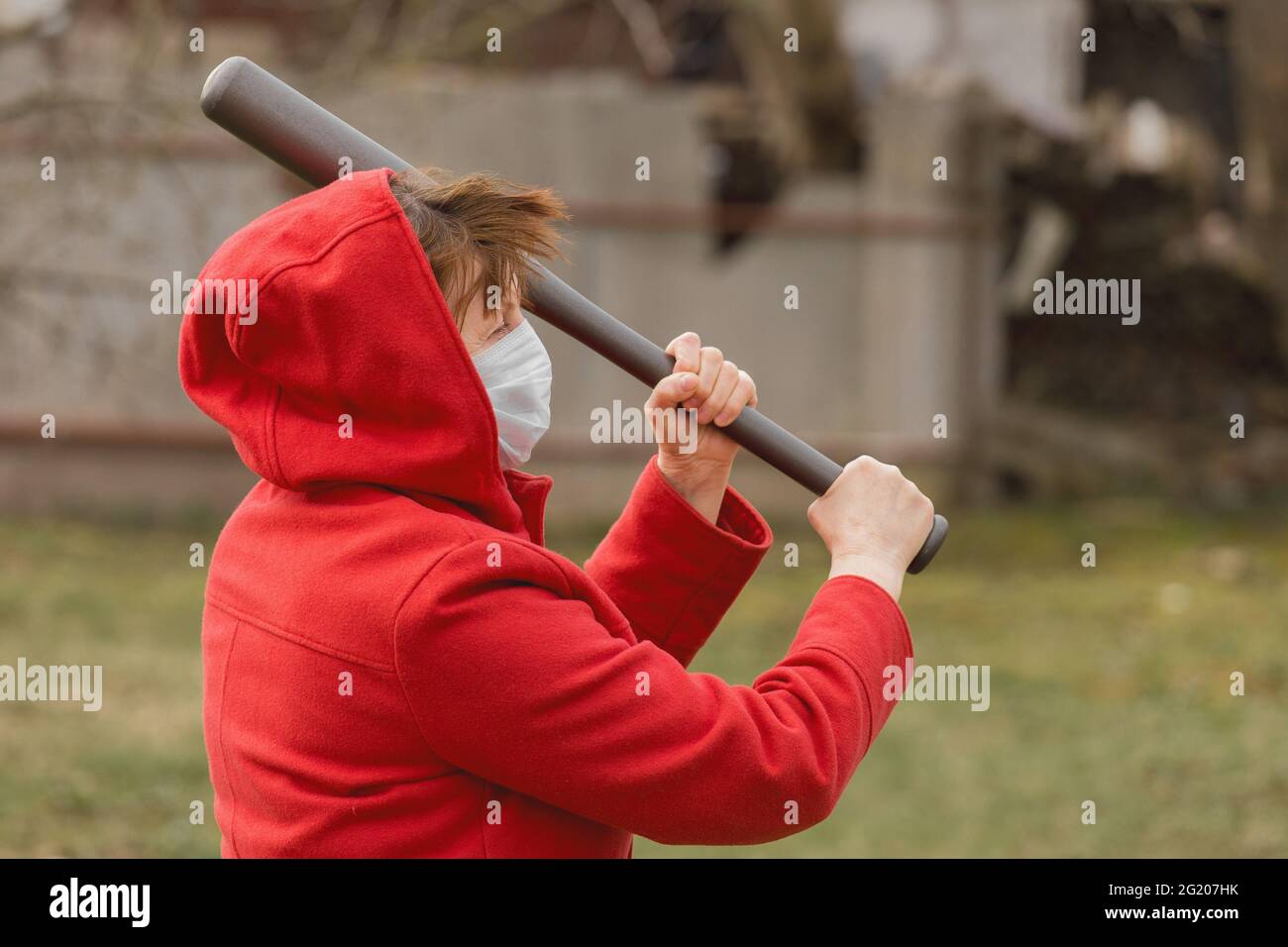 Arrabbiato aggressivo anziano donna in protezione sicuro maschera medica altalena baseball bat sullo sfondo di strada all'aperto, ritratto, primo piano. Foto Stock