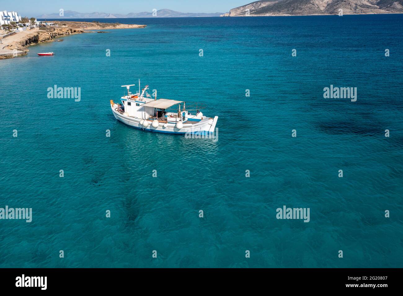 Barca da pesca su sfondo mare turchese di colore blu. Vista aerea del drone. Tradizionale peschereccio ormeggiato in acque calme dell'Egeo, giorno di sole. Grecia, Koufonisi Foto Stock