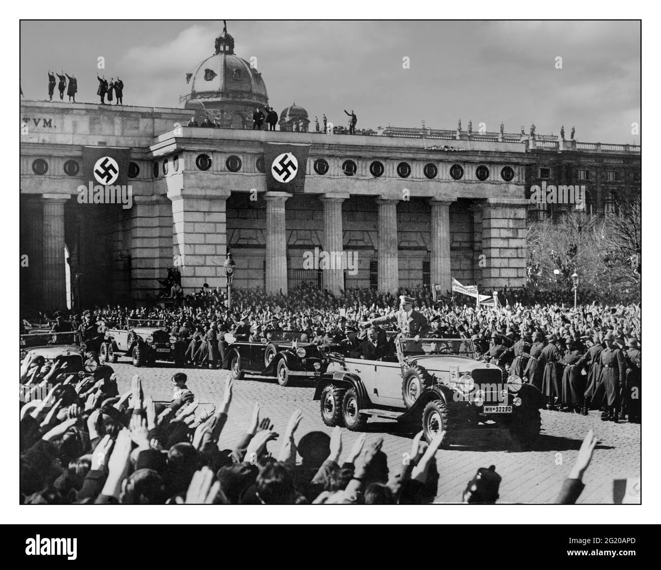 Anschluss Hitler Vienna occupazione il cancelliere tedesco Adolf Hitler (1889 - 1945) è Heil Hitler salutato da folle estatiche mentre guida oltre in 6 ruote tutti i terreni aprono Mercedes ad una cerimonia della sfilata della truppa con bandiere di swastika nell'occupazione nazista Vienna, Austria, 15 marzo 1938. Foto Stock