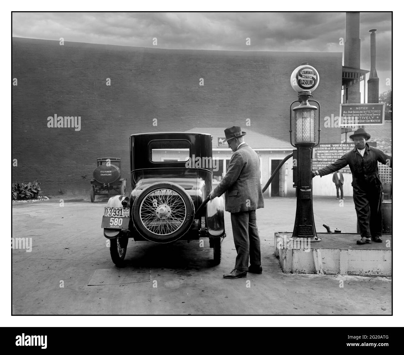 Archivio 1900 benzina benzina benzina benzina benzina benzina uomo rifornimento la sua auto in Un self-service Standard Motor benzina stazione nella zona di Washington D.C. Un cartello indica ai clienti che la benzina è filtrata e non contiene né sporcizia né acqua. 1920. Washington USA Foto Stock