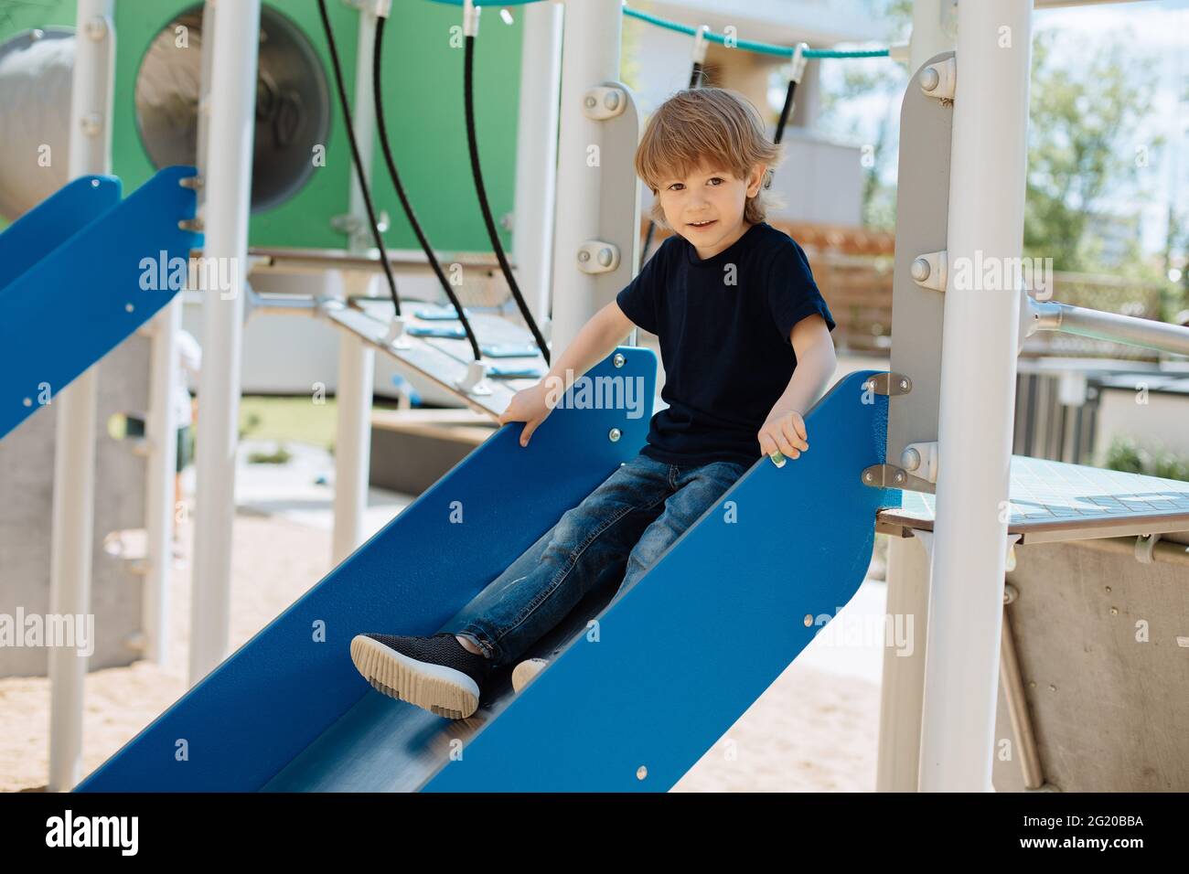 Il bambino di 3 anni si siede sullo scivolo e guarda la camera.concetto di intrattenimento e attività all'aperto per i bambini. Foto Stock