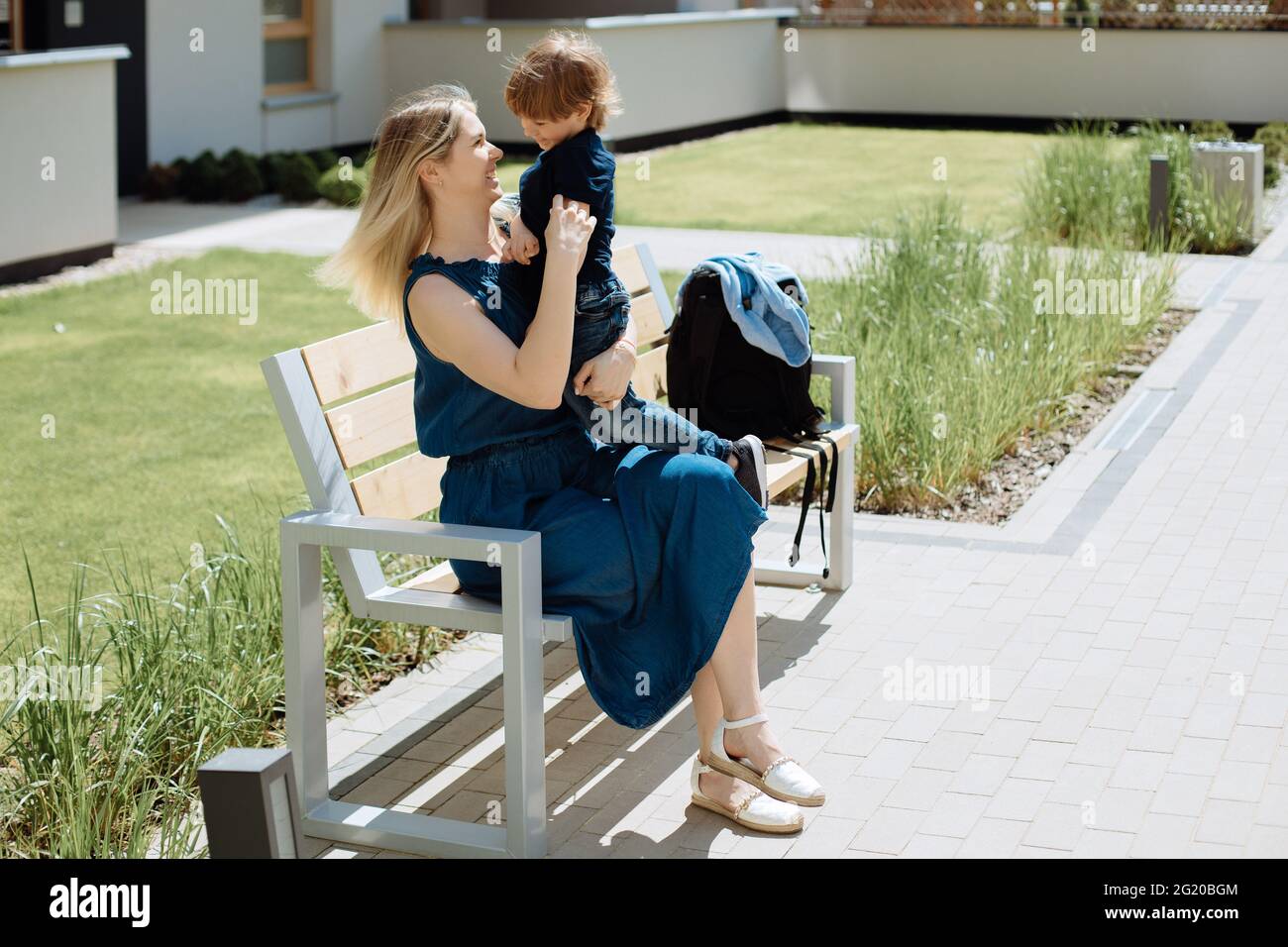 La giovane madre abbracca il figlio di 3 anni seduto su una panchina nel parco. Concetto di amore e affetto Foto Stock