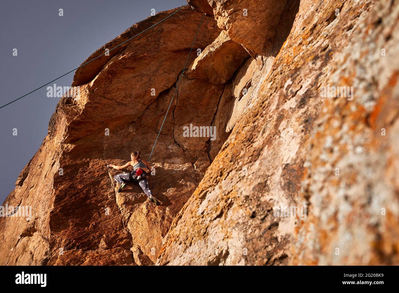 La giovane atleta sta arrampicando sulla roccia alta al tramonto vicino al fiume in Kazakhstan Foto Stock