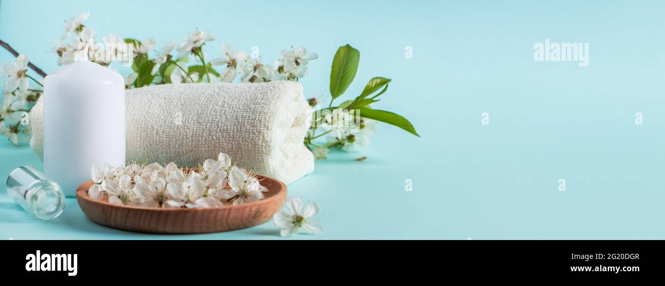 Concetto di benessere aromaterapico. Accessori per il benessere e il relax su sfondo blu. Olio aromatico, asciugamano, candela e fiori. Prodotto organico per la cura della pelle Foto Stock