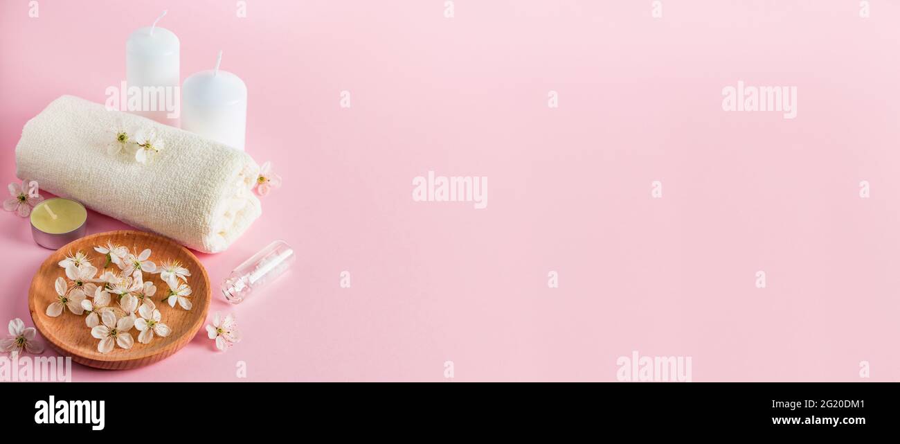 Prodotti cosmetici per spa e aromaterapia. Candele, sale marino, asciugamano e fiori su sfondo rosa. Cura della pelle e concetto di bellezza. Luogo per il vostro te Foto Stock