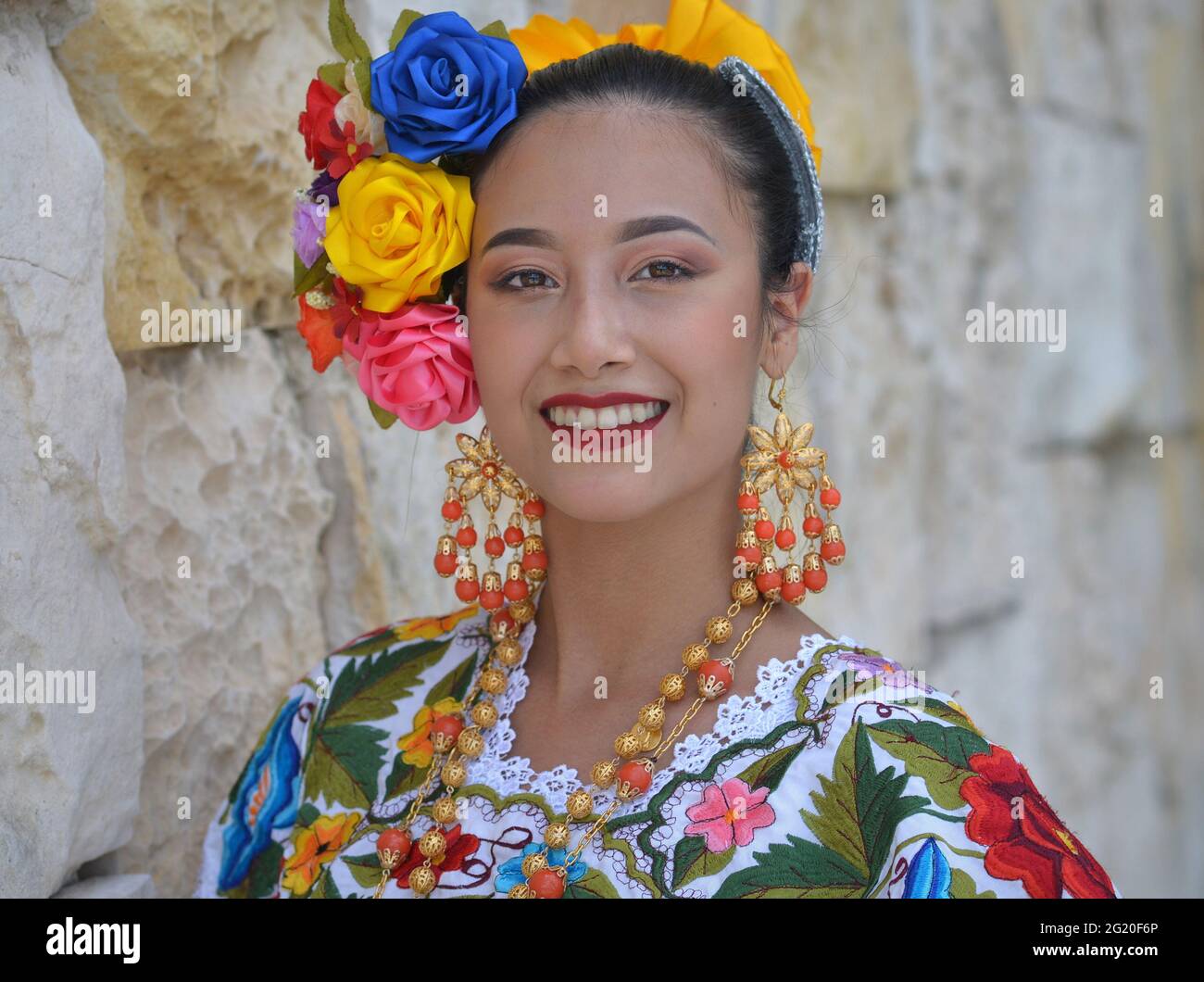 Giovane bella donna messicana con trucco indossa tradizionali Yucatecan Yucatecan abito folclorico con fiori nei capelli e sorrisi per la macchina fotografica. Foto Stock