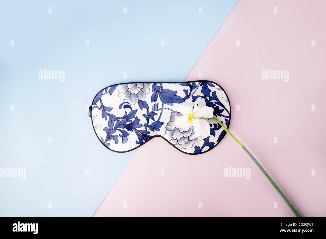 Bella maschera di sonno di seta per gli occhi con motivi floreali e narciso bianco o fiore di daffodil su uno sfondo blu rosa Foto Stock