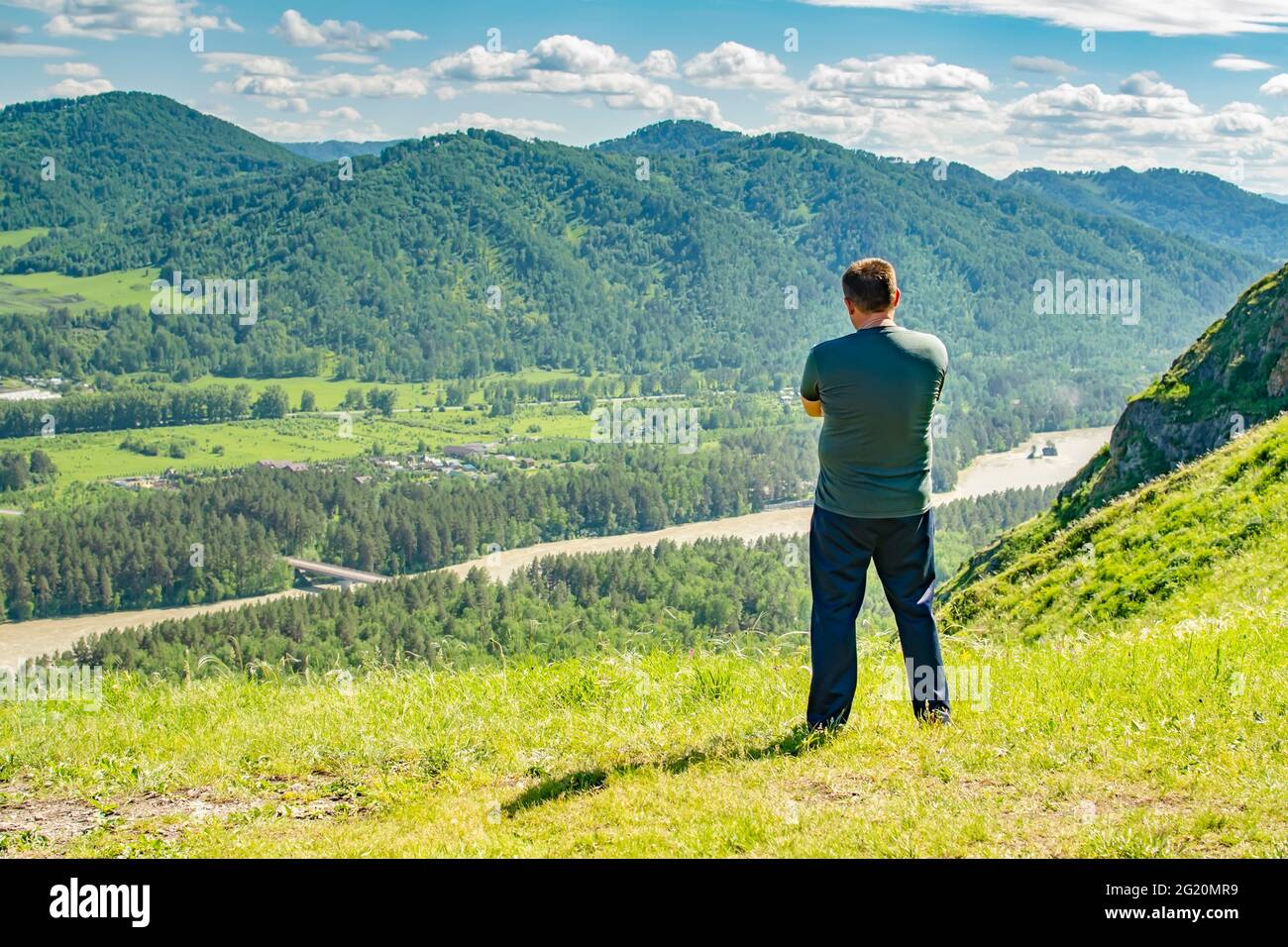 un uomo si erge sulla cima di una montagna e guarda con attenzione ad una valle montana con un fiume Foto Stock