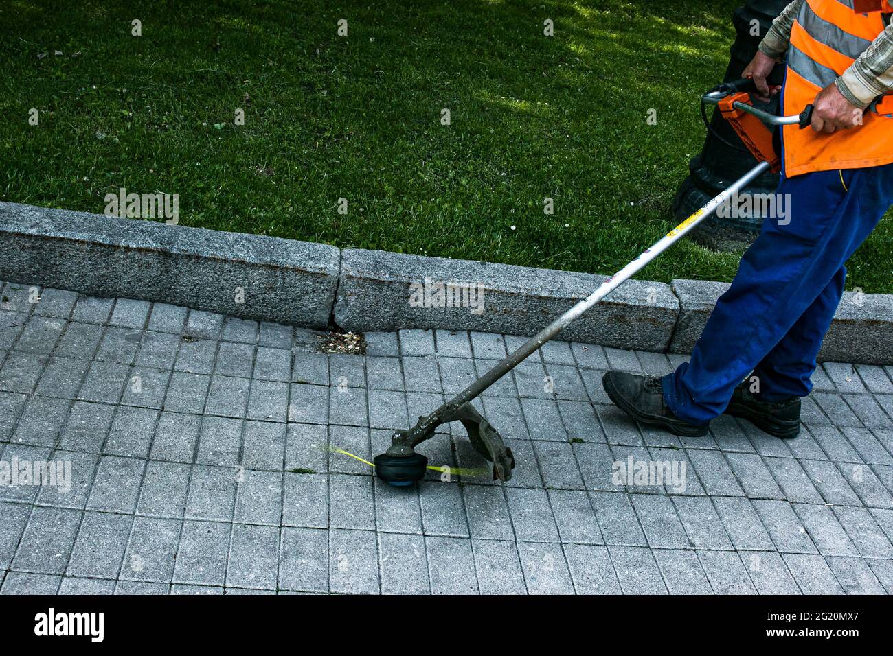 Un operaio in tute con un trimero in mano taglia l'erba sul prato e sentieri nel parco. Cura del territorio. Foto Stock