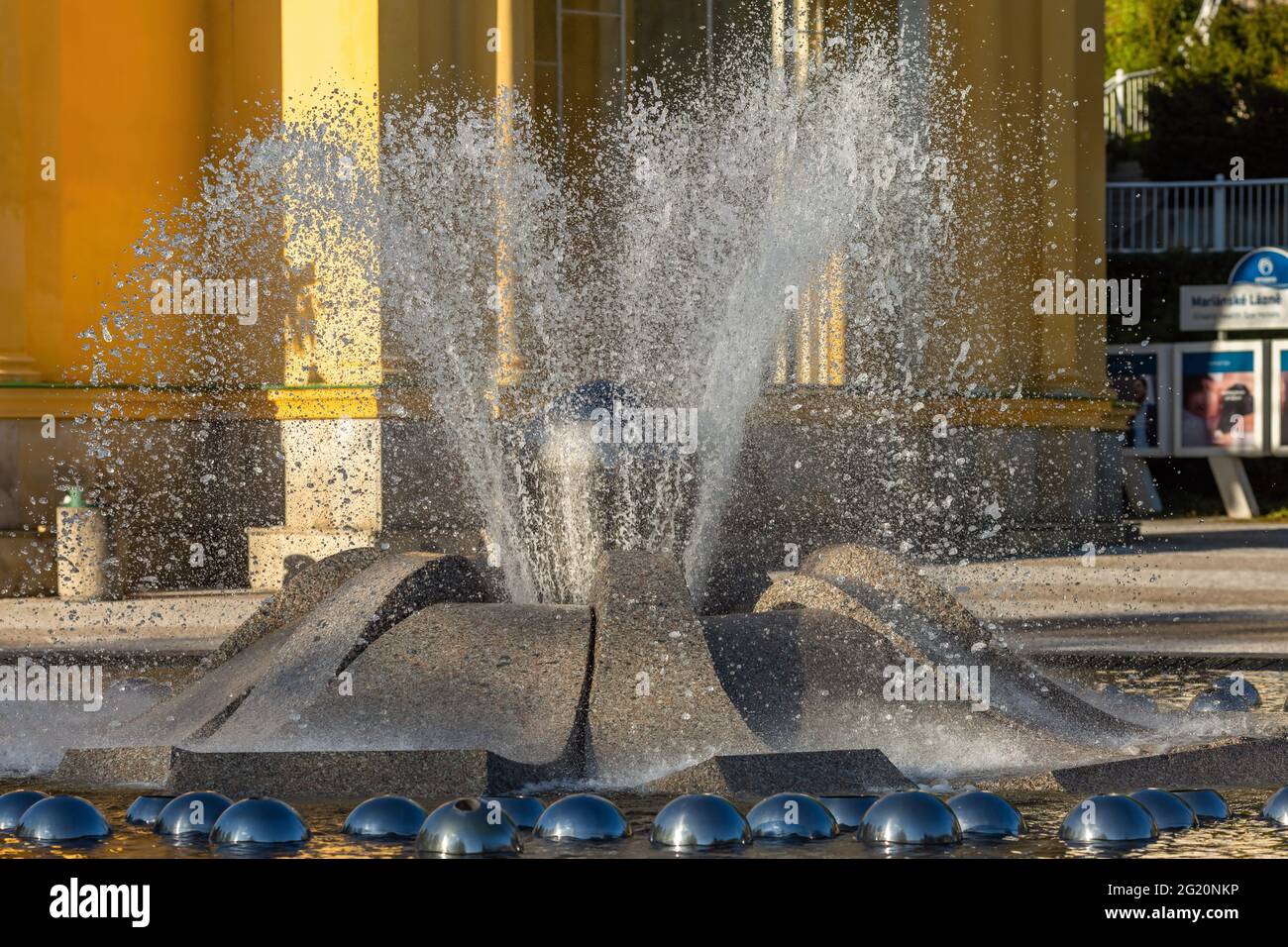 Marianske Lazne, Repubblica Ceca - Maggio 30 2021: Vista ravvicinata della fontana d'acqua. Edificio giallo colonnato sullo sfondo. Spa città. Foto Stock