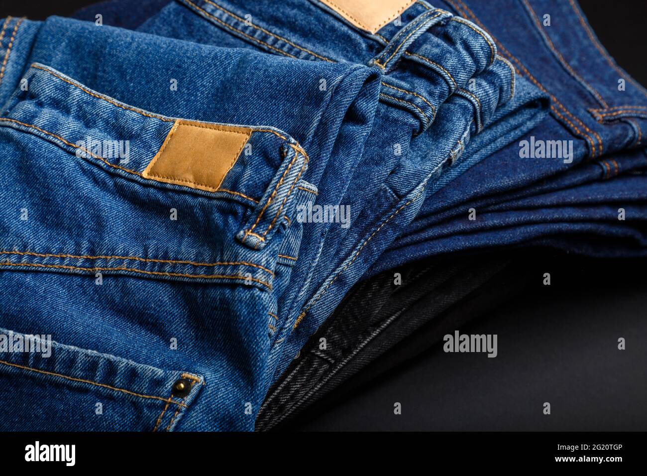 Pantaloni in denim jean piegati in pila con etichetta mockup vuota marrone. Jeans casual blu accatastati in pile su sfondo nero. Foto Stock