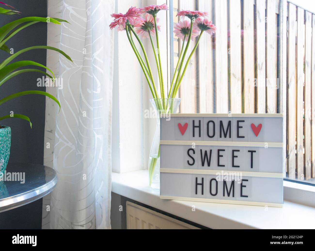Segno Home dolce home testo su lightbox ,Windowsill vicino finestra con fiori rosa, cornice decorativa sfondo moderno interno, casa elegante accogliente Foto Stock
