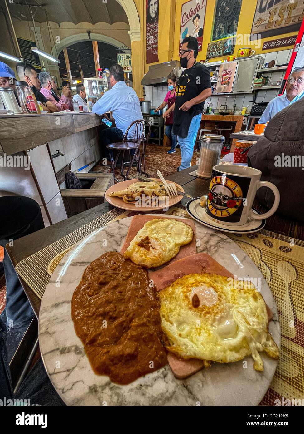 Due uova strapazzate su fette di prosciutto, fagioli e caffè americano in una tazza Guns and Roses al Cafe Cele nel mercato municipale di Hermosillo, Messico. Colazione, cibo, cibo, pasti, cibo. (Foto di Luis Gutierrez / Norte Photo) Dos huevos estrellados sobre rebanadas de jamon, frijoles y cafe americano en tasa de Guns and Roses en el Cafe Cele del mercado Municipal de Hermosillo, Messico. Desayuno, Alimentos, comida, Comidas, cibo. (Foto di Luis Gutierrez/ Norte Photo) Foto Stock