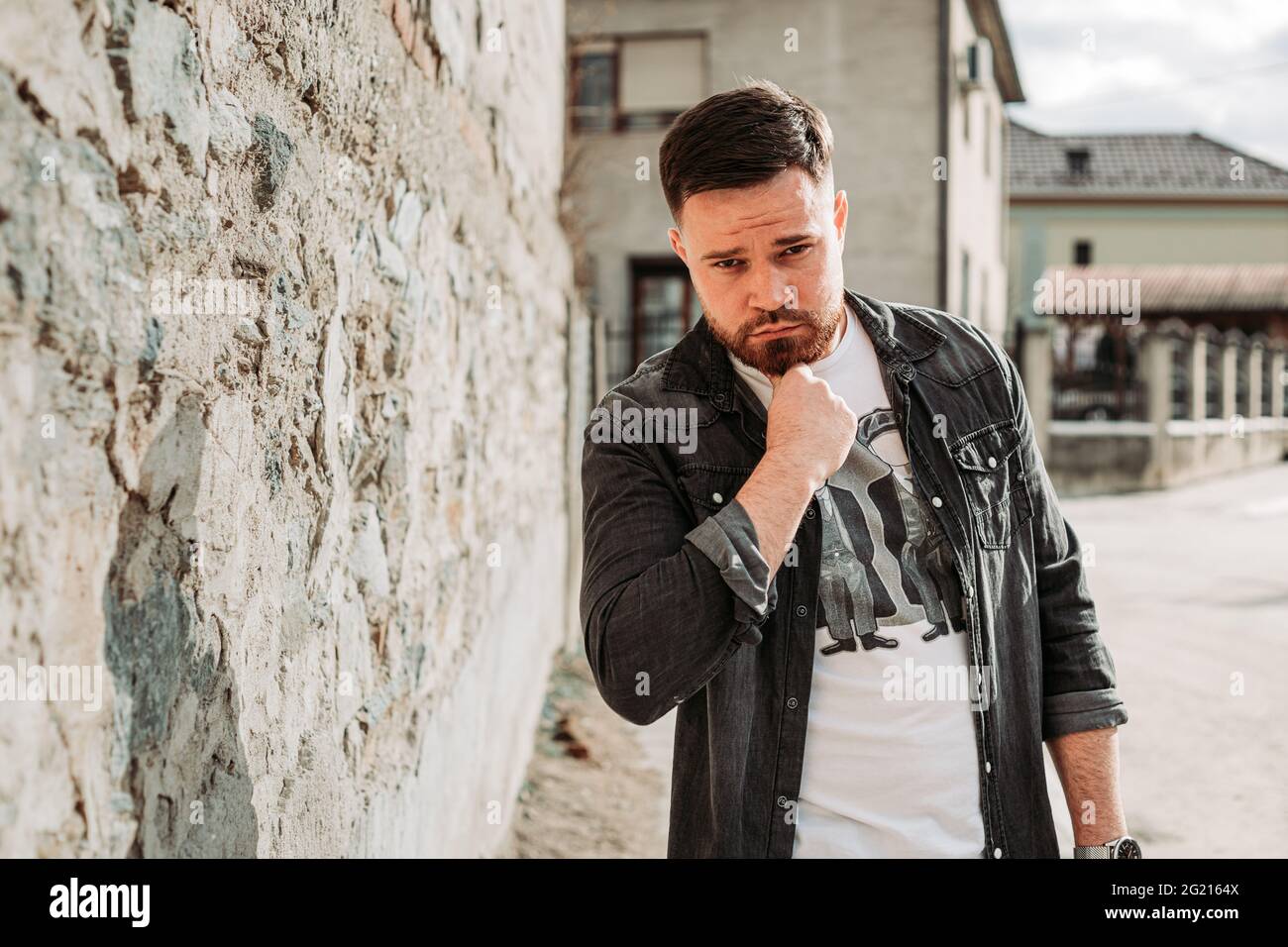 Ragazzo giovane, hipster che tiene la mano sotto il mento, pensando Foto Stock