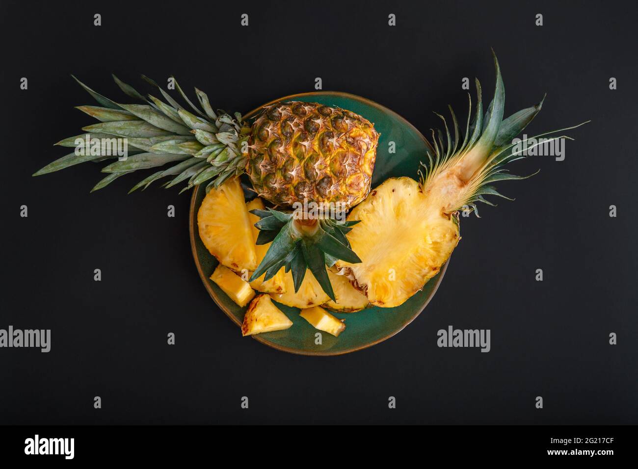 Ananas a fette. Bromelina ananas intero tropicale frutta estate metà ananas nero sfondo scuro su piatto verde. Dessert di frutta estiva vista dall'alto Foto Stock