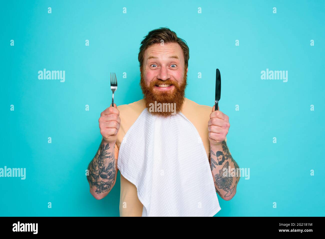 L'uomo felice con i tatuaggi è pronto a mangiare con le posate in mano Foto Stock