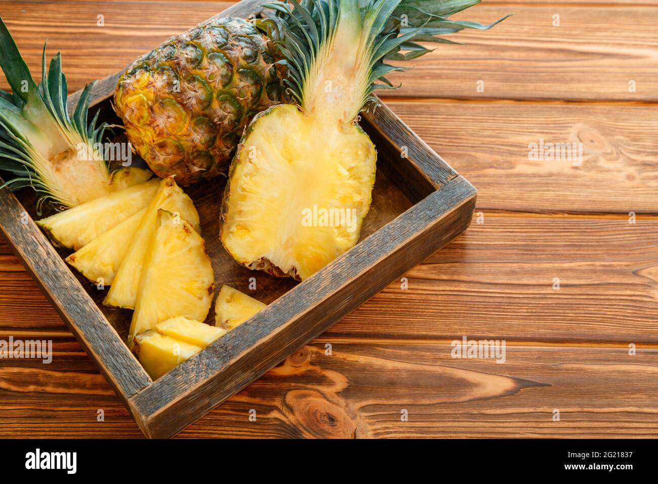 Ananas a fette. Bromelain tropicale frutta estate ananas metà e ananas intero su tavola marrone scuro in scatola di legno con spazio di copia Foto Stock