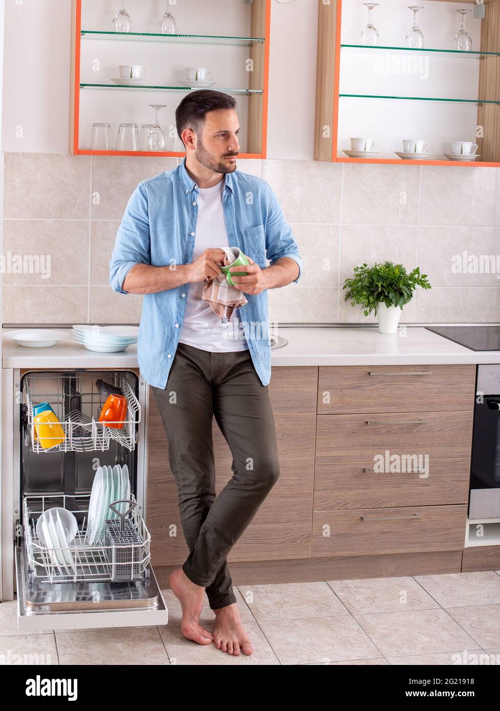Serio giovane uomo in cucina che fa lavoro domestico. Tazza per lucidatura  uomo accanto alla lavastoviglie Foto stock - Alamy