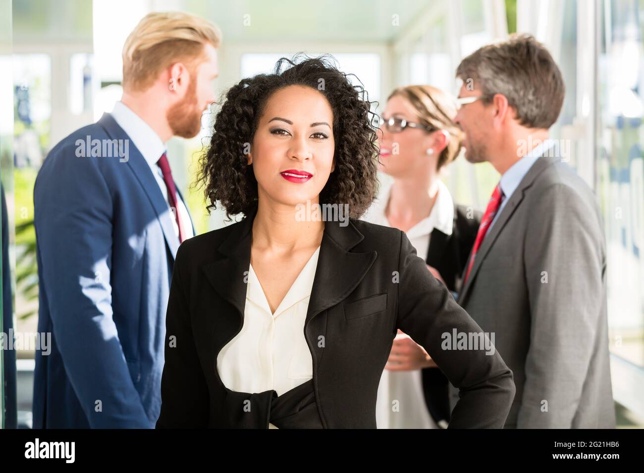 Imprenditrice in piedi con la mano sulla sua anca, con i suoi collaboratori parlano in background Foto Stock