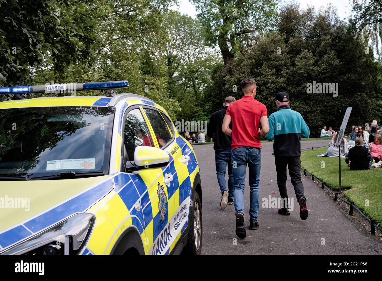 Tre giovani passano da un'auto di polizia al parco verde di Stephen durante il fine settimana delle feste della Banca. Dall'aprile 2021, Dublino ha gradualmente attenuato le restrizioni, e con la festa della banca in calo lunedì 7 giugno, il riscaldamento del tempo, e i servizi igienici pubblici installati nelle strade, diverse persone hanno scelto di trascorrere il fine settimana socializzando all'aperto nel centro della città. La grande folla ha provocato tensioni come le bottiglie che sono state gettate alla polizia, le persone che si rifiutano di trasferirsi quando la polizia li ha richiesti, e altri incidenti che hanno portato a 47 arresti fino ad oggi. Foto Stock