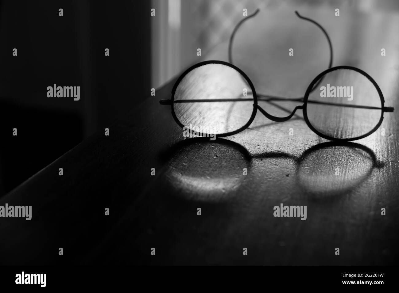 Un vecchio modello di occhiali vintage con montature in filo metallico con  luce che brilla su un vecchio tavolo in legno in bianco e nero con  profondità bassa o Foto stock -