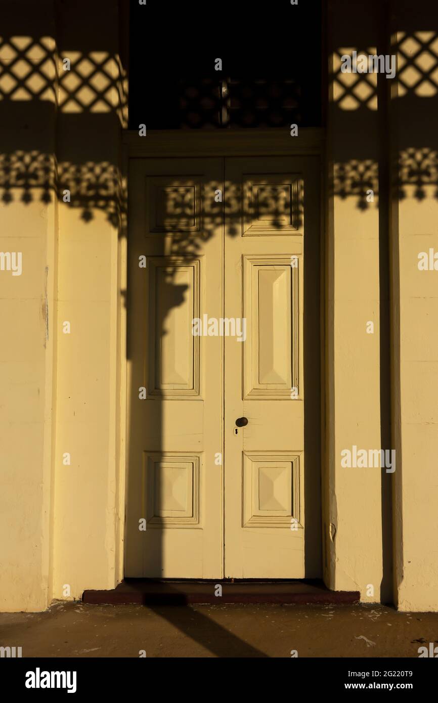Una porta in vecchio stile con eleganti ombre proiettate dal sole della mattina presto che splende attraverso finiture in ghisa su un vecchio edificio. Foto Stock