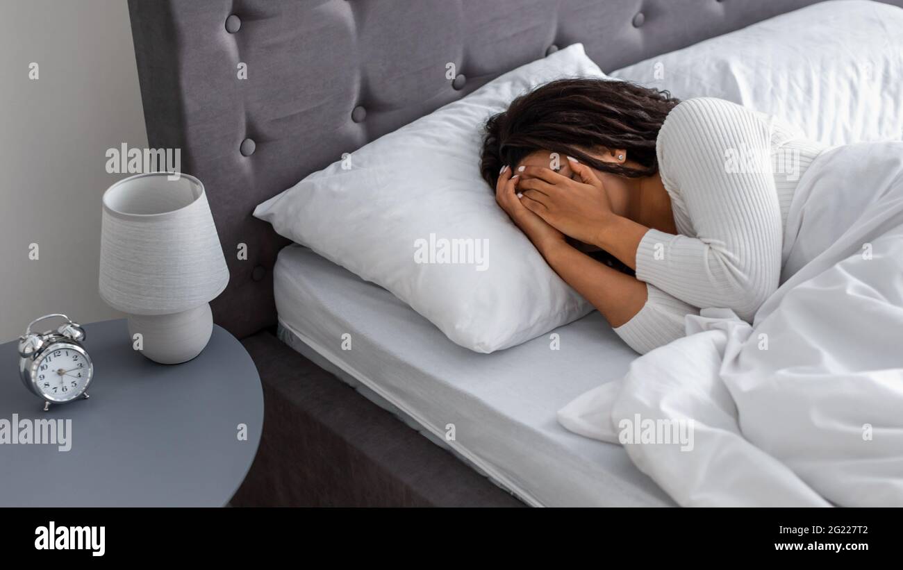 Donna nera che piange, sdraiata nella faccia di copertura del letto Foto Stock
