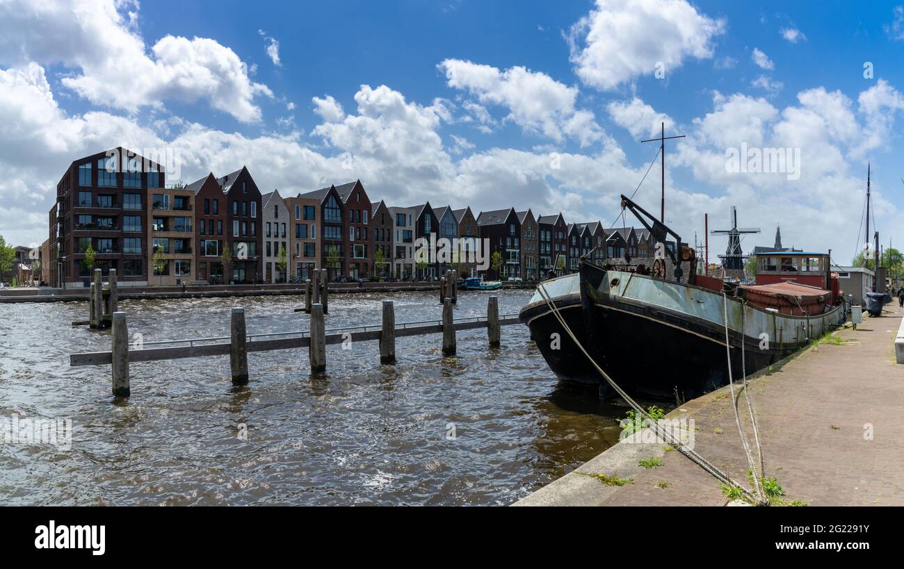 Haarlem, Paesi Bassi - 21 maggio 2021: Fila di case colorate sui canali di Haarlem con una vecchia chiatta fluviale in primo piano Foto Stock