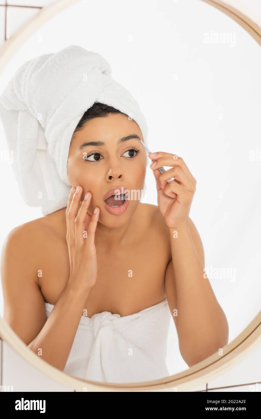 giovane donna afro-americana spaventata con sopracciglia a bocca aperta con pinzette in bagno Foto Stock