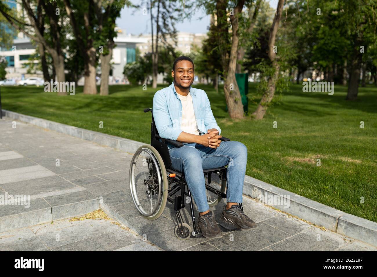 Ambiente accessibile ai disabili. Felice ragazzo nero in sedia a rotelle scendendo rampa sulla strada della città Foto Stock