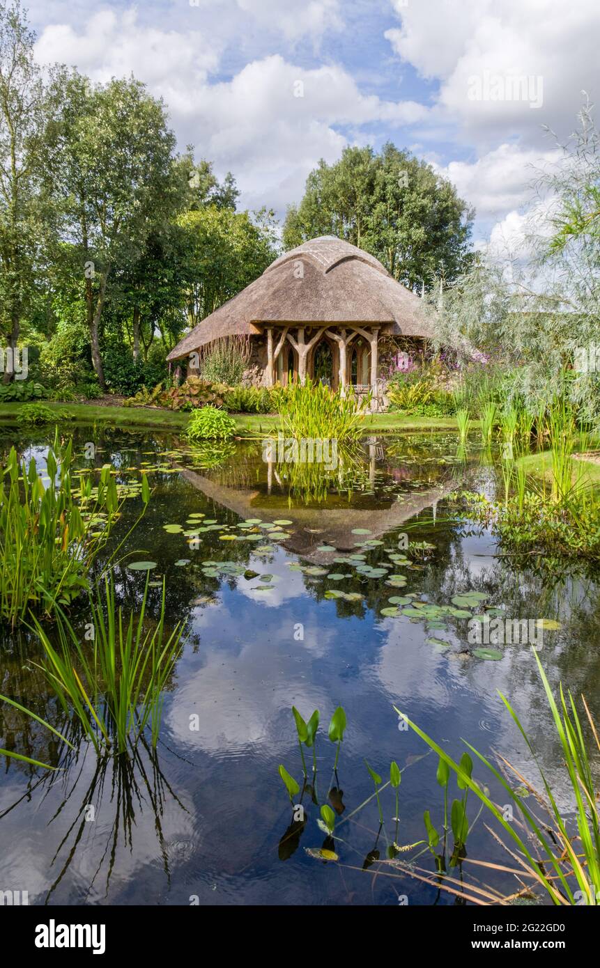 Un arbour di paglia che si affaccia su un antico laghetto di pesci nei giardini del Menagerie, Horton, Northamptonshire, UK; aperto sotto il National Garden Scheme Foto Stock